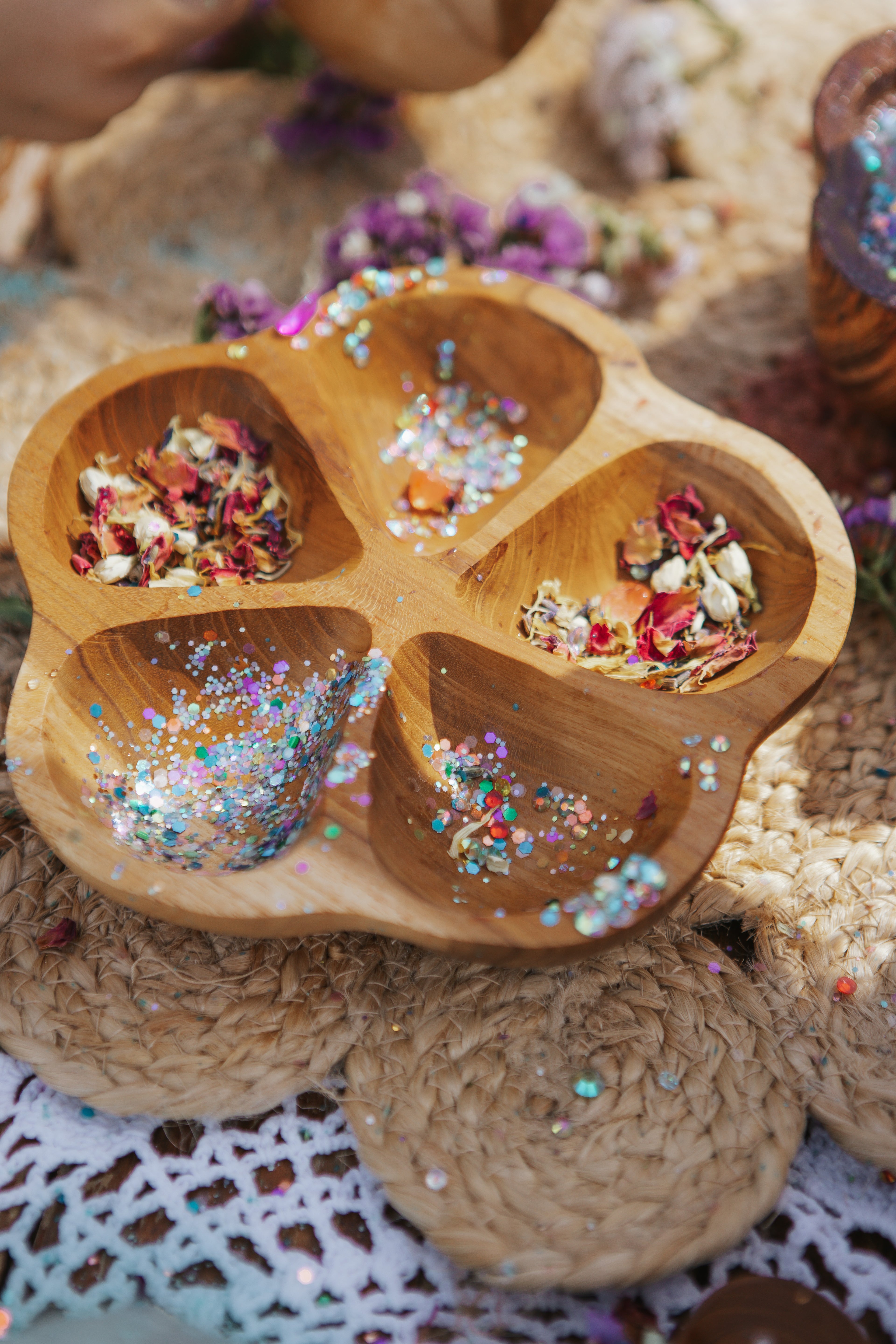 Wooden bowl with compartments filled with bio glitter, and dried flowers on a sensory play table